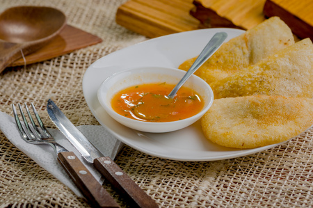 Three empanadas nicely arranged on white platter next to small salsa bowl and rustic background .の写真素材