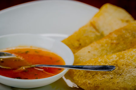 White plate with three delicious empanadas lined up and small bowl of red salsa on top.の写真素材