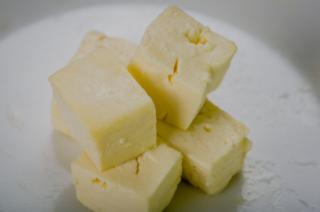 Closeup stable of fresh cheese cut into square pieces on white surface.の写真素材