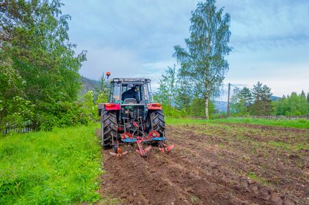 OSLO, NORWAY - 8 JULY, 2015: Tractor working in field opening preparing soil for planting vegetables, shot from behind angle.のeditorial素材