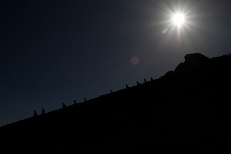 Silhouettes of hikers going downhill in a mountain with bright sun in the background