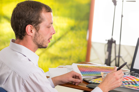 Man working on laptop while holding up pantone palette, colormap from behind angle.  Concept graphic...