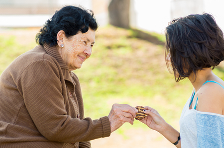 Lovely hispanic grandmother and granddaughter enjoying quality time outdoors sharing snacks.の写真素材