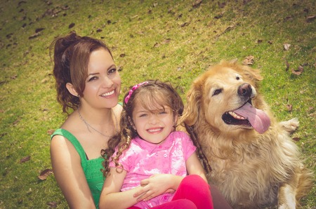 Mother, daughter and golden retriever dog sitting outside in park environment laughing and enjoying .の写真素材