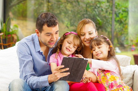 Family portrait of father, mother and two daughters sitting together in sofa playing happily with...