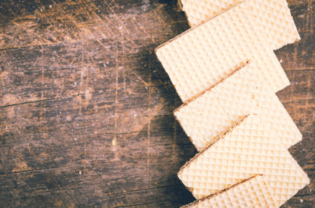 Closeup square cookies lying overlapping each other in a row across wooden surface.