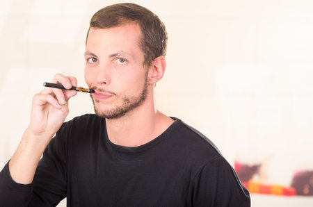 Hispanic man wearing dark sweater enjoying an electronic cigarette while posing for camera.