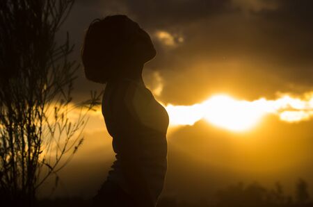 Teenage girl posing with sunset behind clouds in background creating spectacular colors, silhouette concept.の写真素材