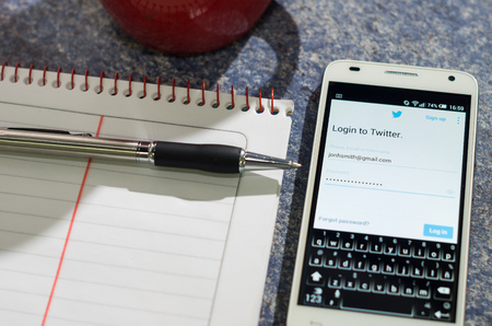 QUITO, ECUADOR - AUGUST 3, 2015: White smartphone lying on table with Twitter website screen open next to a pen, notepad and coffee mug, business communication concept.のeditorial素材