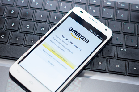 QUITO, ECUADOR - AUGUST 3, 2015: White smartphone closeup lying on laptop keyboard with Amazon website screen visible.のeditorial素材