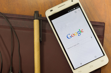 QUITO, ECUADOR - AUGUST 3, 2015: White smartphone lying on desk with Google screen open next to a pen, business and communication concept.のeditorial素材