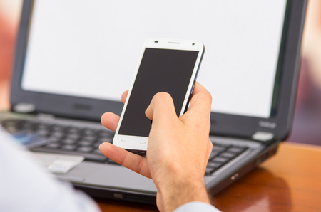 QUITO, ECUADOR - AUGUST 3, 2015: Closeup of young man hands holding smartphone with laptop computer in front.のeditorial素材