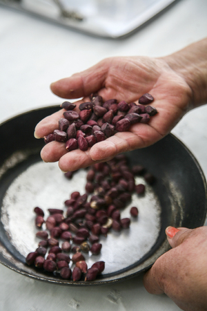 Hand holding up palm of black beans over frying pan with more of same vegetable, preparing fanesca concept.の写真素材