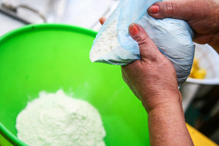 Two hands holding bag of flour while puring into green plastic bowl, preparing fanesca concept.