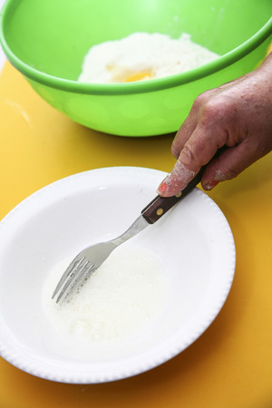 Hand with fork whiiping eggwhites in white small bowl, preparing fanesca concept.の写真素材