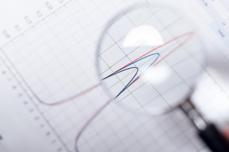 Closeup magnifying glass over paper with red and blue graph visible.の写真素材