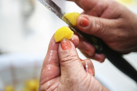 Hands holding knife and cutting olluco vegetable in halfs, preparing fanesca concept.の写真素材
