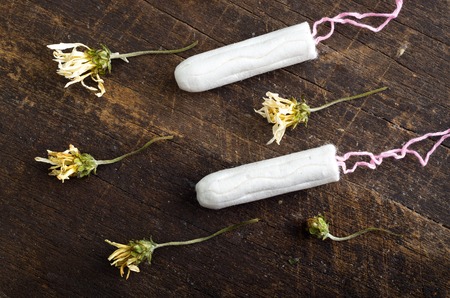 Clean white tampons lying on wooden surface with yellow colored dry flowers around.の写真素材