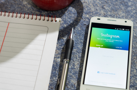 QUITO, ECUADOR - AUGUST 3, 2015: White smartphone lying on table with Instagram website screen open next to a pen, notepad and coffee mug, business communication concept.のeditorial素材