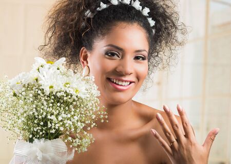 Portrait of beautiful exotic latin bride wearing white dress and holding flower bouquet showing wedding ringの写真素材
