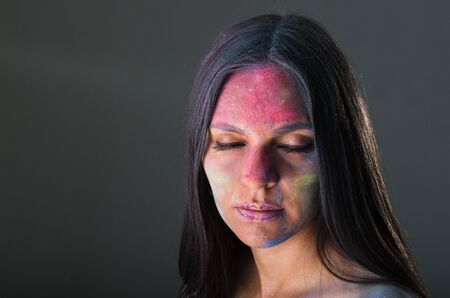 Close up portrait of beautiful mysterious young latin girl with colored powder on her face closing her eyesの写真素材