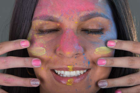 Beautiful happy young brunette girl painting her face with colorful powderの写真素材
