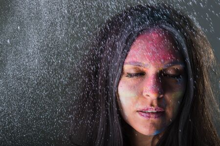 Close up portrait of beautiful mysterious young latin girl with colored powder on her face closing her eyesの写真素材