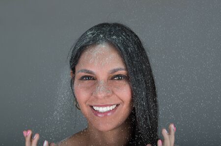 Portrait of beautiful smiling brunette girl as colorful powder falls down on her faceの写真素材