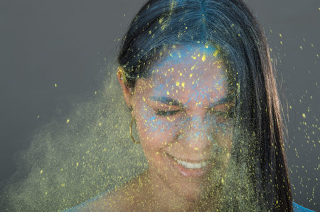 Beautiful young brunette girl with colorful powder blowing in her face