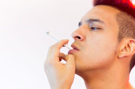 Hispanic male headshot posing with serious facial expression and smoking a cigarette.