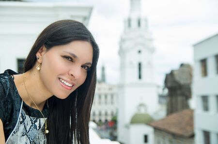 Classy attractive brunette wearing black white dress in urban environment leaning on surface and enjoying a view while smiling.の写真素材