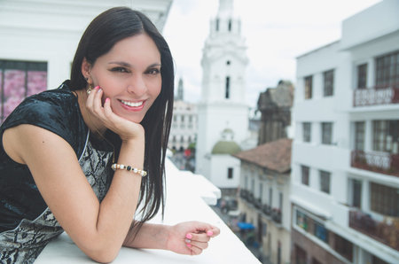 Classy attractive brunette wearing black white dress in urban environment leaning on surface and enjoying a view while smiling.の写真素材