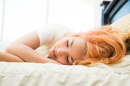 Pretty young woman lying cozy in bed posing for camera.の写真素材