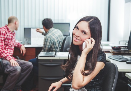 Hispanic brunette sitting by office desk talking on telephone smiling with positive attitude.の写真素材