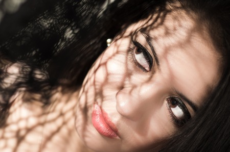 Headshot brunette model using patterned shadows as artistic effect on face while posing.の写真素材