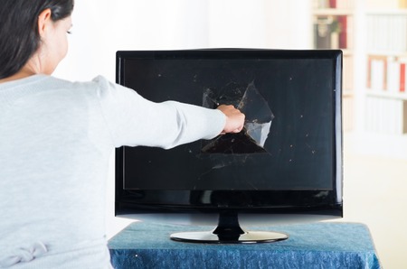 Brunette female punching fist into broken computer screen.の写真素材