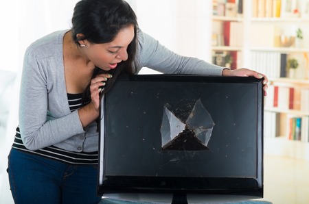 Brunette female looking over broken computer screen with shocked facial expression on her face.の写真素材
