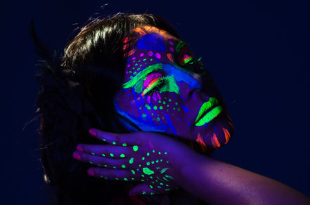 Headshot woman wearing awesome glow in dark facial paint, blue based with other neon colors and...
