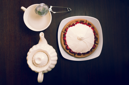 Cup of tea, hot water decanter and beautiful small pie covered with wild berries under cream layer, elegant concept.の写真素材