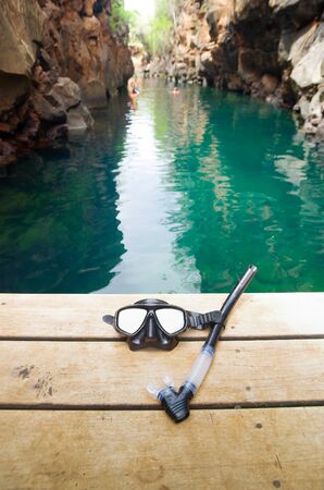 Diving mask and snorkel lying on wooden pier with beautiful green ocean water sorrounded by spectacular rock cliffs both sides, Galapagos Islands Ecuador.の写真素材