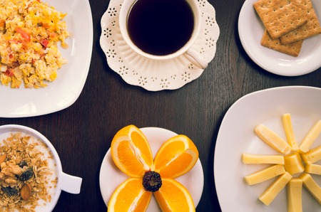 Elegant breakfast concept seen from above, coffee cup, sliced cheese, oranges, crackers and bowl with youghurt granola.の写真素材