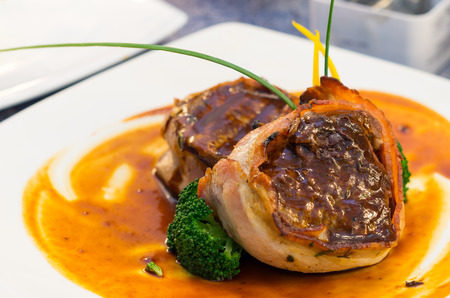 Delicious tenderloin steak wrapped in bacon and cooked to perfection, placed on orange plate with some vegetable elements, elegant presentation.の写真素材