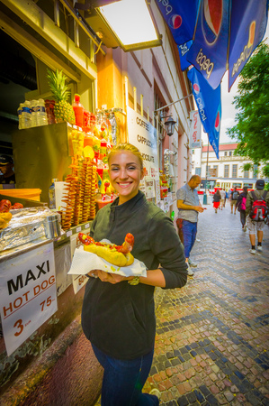 Prague, Czech Republic - 13 August, 2015: Pretty blonde local girl holding up a giant bratwurst sausage in bread and smiling to camera.のeditorial素材