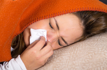 Brunette lying down under orange blanket and blowing her nose, sick with flu concept,