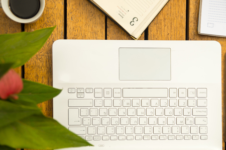 White laptop, notepad and coffee cup as seen from above sitting on wooden surface.の写真素材