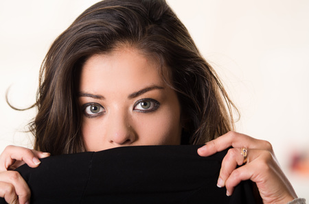 Headshot attractive brunette facing camera covering half her face with black clothing, white studio background.の写真素材