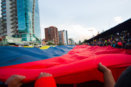 Quito, Ecuador - April 7, 2016: Group of people displaying a very big Ecuadorian Flag, protest signs, and journalists during anti government protests in Shyris Avenueのeditorial素材
