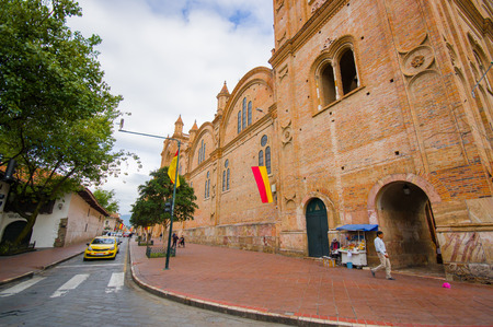 Cuenca, Ecuador - April 22, 2015: Large and beautiful old brick facade of main cathedral stretching along city blocks with people walking.のeditorial素材
