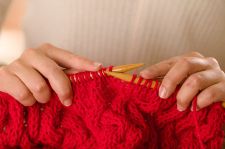 Closeup womans hands holding wooden knitting needles working on red scarf.