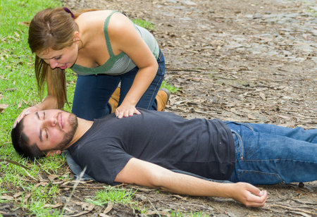 Young man lying down with medical emergency, young woman sitting by his side performing light...
